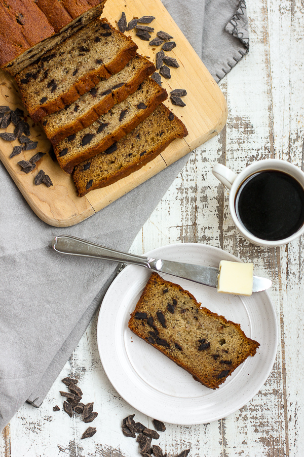 slices of banana bread on a cutting board and one piece is served on a plate with butter and coffee