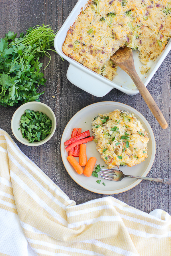 Cheesy chicken and broccoli being served from the casserole dish and on a dinner plate served with carrots and red bell peppers