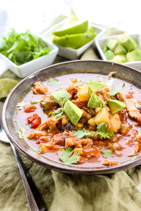 The chili in a serving bowl with cilantro, lime and avocado garnished in the background in small serving bowls