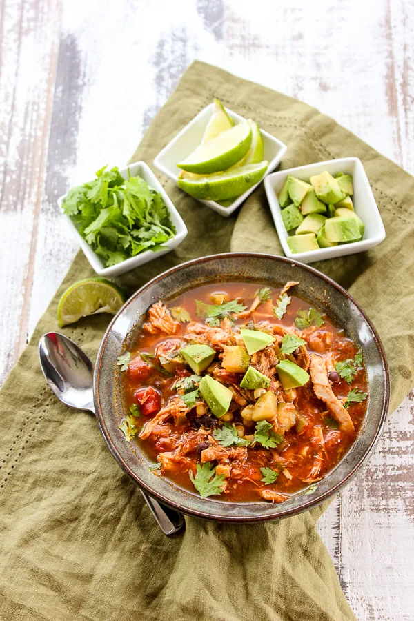 Overhead shot of chicken chili with all of the garnishes, lime, cilantro and avocado