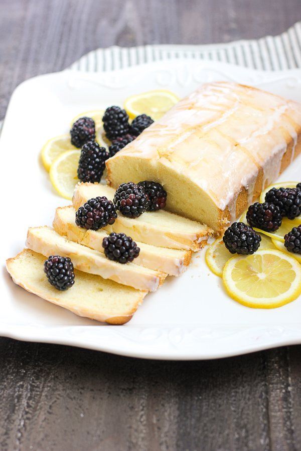 Glazed lemon pound cake sliced and served with blackberries and garnished with lemon slices
