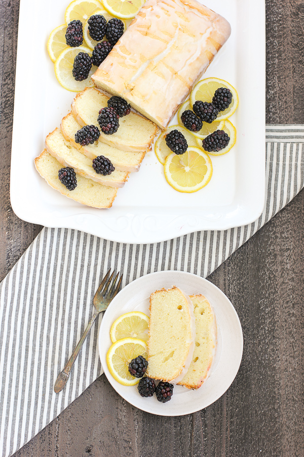 glazed lemon pound cake on a serving platter as well as shown being served on a plate with blackberries ad lemon slices