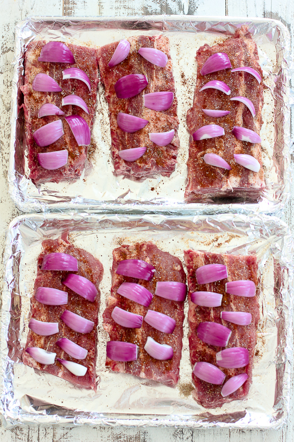 The baby back ribs on foil covered sheet pans topped with onions before going into the oven