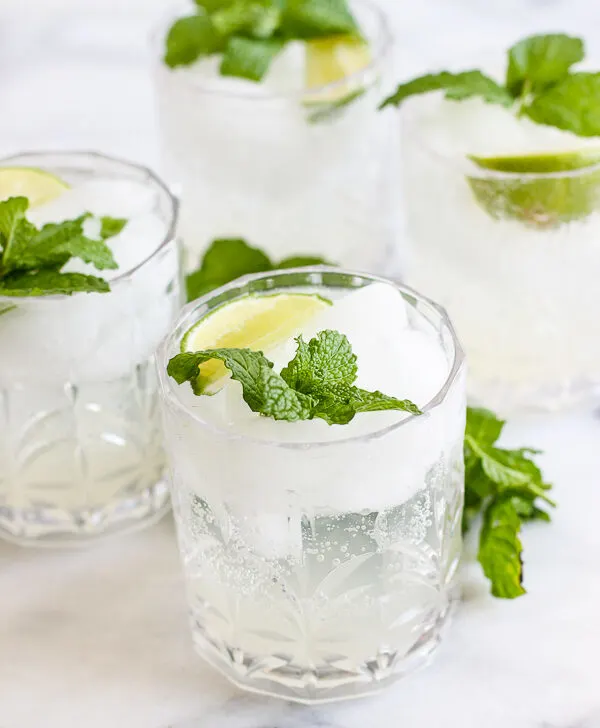 4 mojitos in cocktail glasses garnished with mint and lime