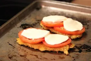 Chicken caprese topped with sliced fresh tomato and fresh mozzarella on a sheet pan ready to be broiled to melt the cheese