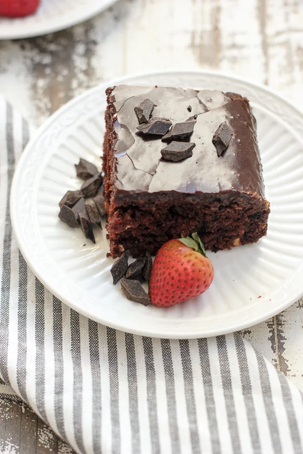A slice of Wacky Cake on a plate garnished with a strawberry and chocolate chunks