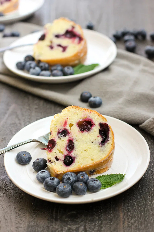 a closer shot of the cake sliced and served on plates with fresh blueberries and mint