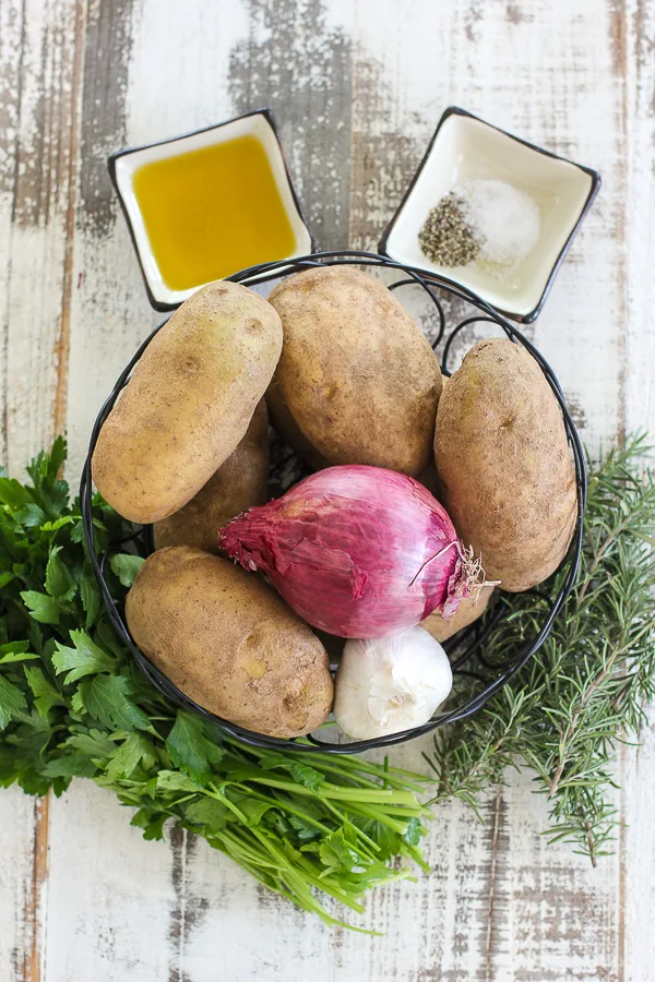 The ingredients needed to make the potato recipe. Russet potatoes, red onion, fresh garlic, rosemary, parsley, olive oil, salt and pepper.