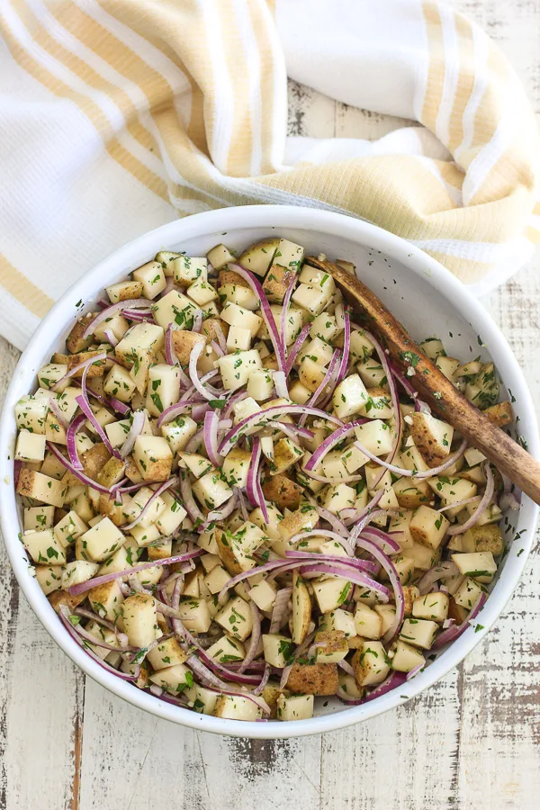 The potatoes in a mixing bowl tossed with the onion and herbs.