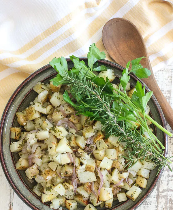 Overhead photo of grill potatoes in the serving bowl garlshed with fresh parsley and rosemary