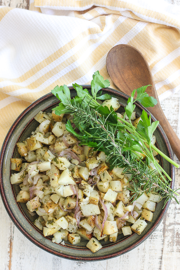 Overhead photo of grill potatoes in the serving bowl garlshed with fresh parsley and rosemary