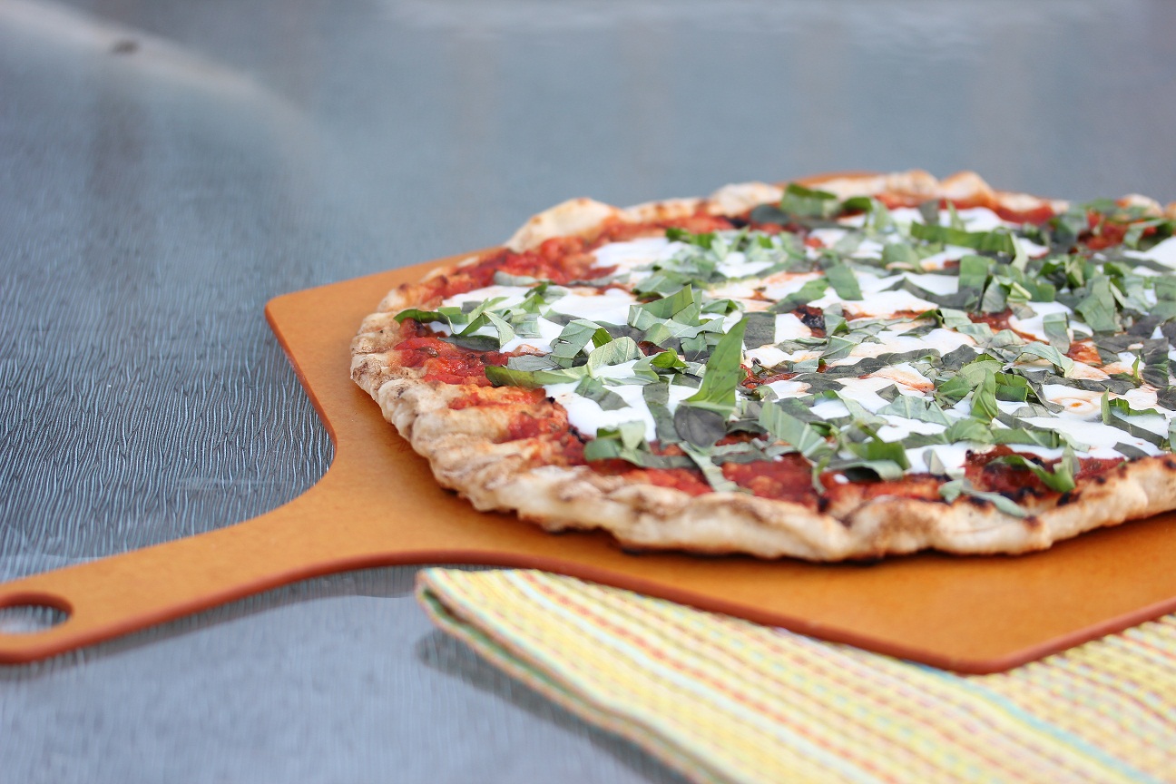 whole grilled Margherita pizza on a pizza peel