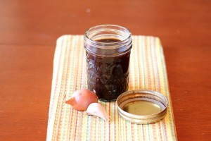 Finished balsamic vinaigrette in a mason jar pictured with a shallot and garlic clove