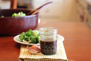 Balsamic vinaigrette in a mason jar pictured with plated salad and serving bowl