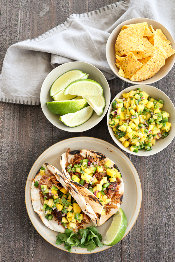 Overhead view of plated pulled pork tacos with extra lime, salsa and tortilla chips