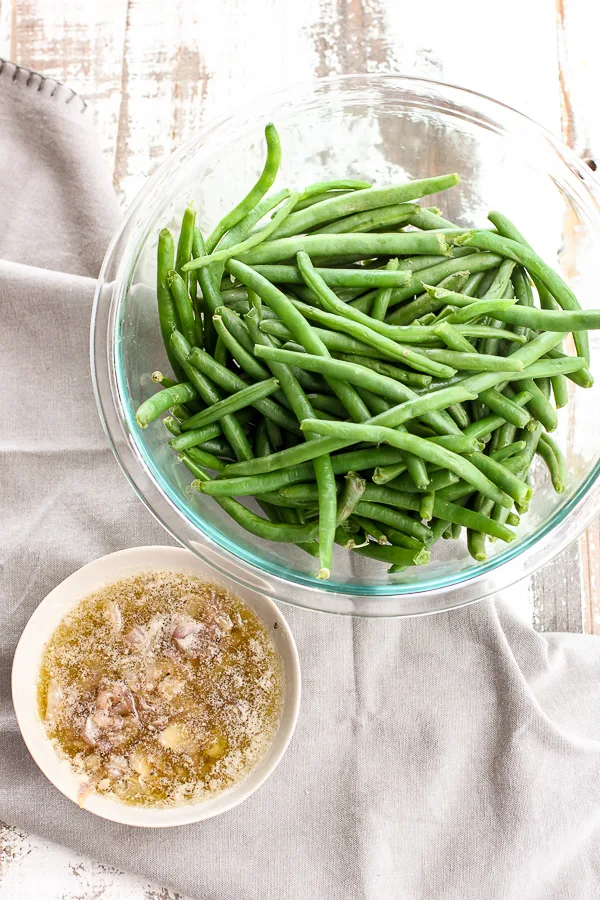 Greens beans in a mixing bowl and shallot brown butter sauce in a separate small bowl