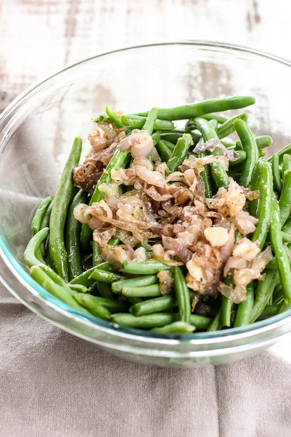 Steamed green beans topped with shallot butter sauce in a mixing bowl