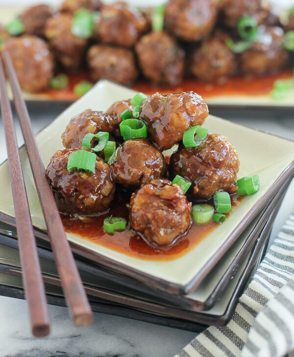 Asian Sweet and sour Meatballs plated on a square plate with chopsticks, with the serving dish with meatballs in the background