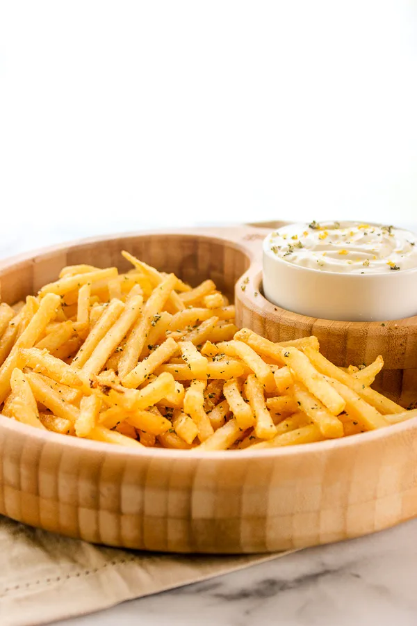 Rosemary garlic fries i a wooden serving bowl served with the lemon dipping sauce