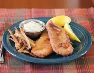 Beer battered tilapia plated with french fries, tartar sauce and lemon wedges