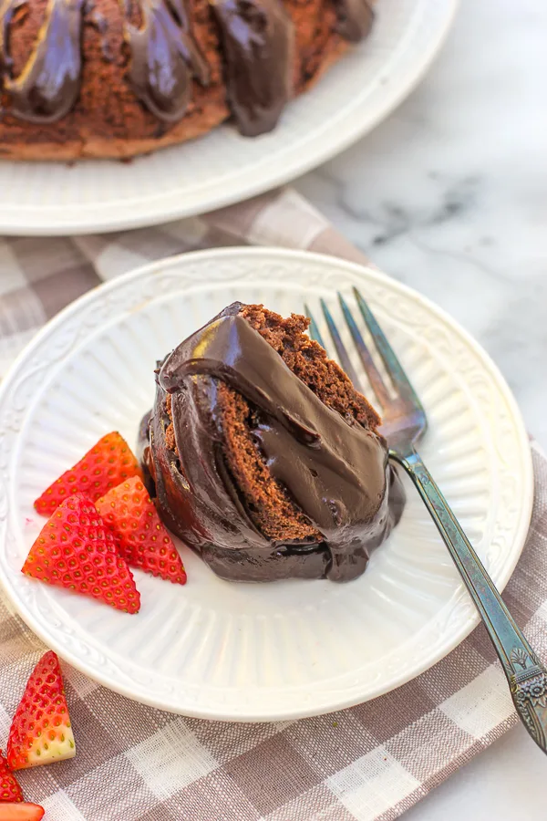 Plated slice of Chocolate Bundt Cake with hot fudge sauce on top and garnished with strawberries