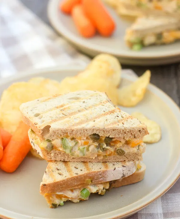 Finished panini cut in half and on a plate with chips and baby carrots