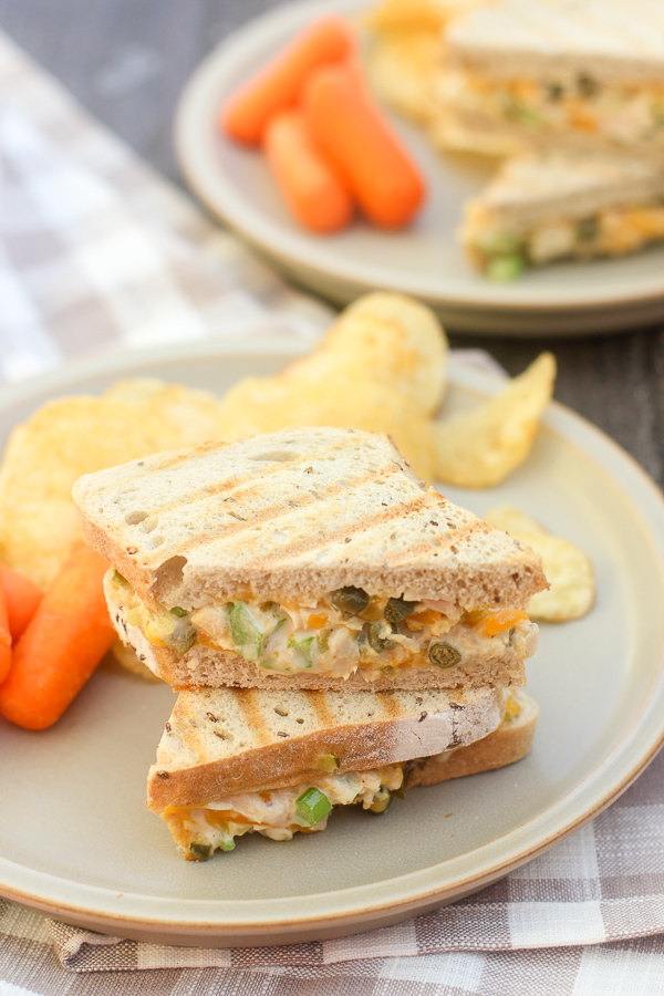 Finished panini cut in half and on a plate with chips and baby carrots