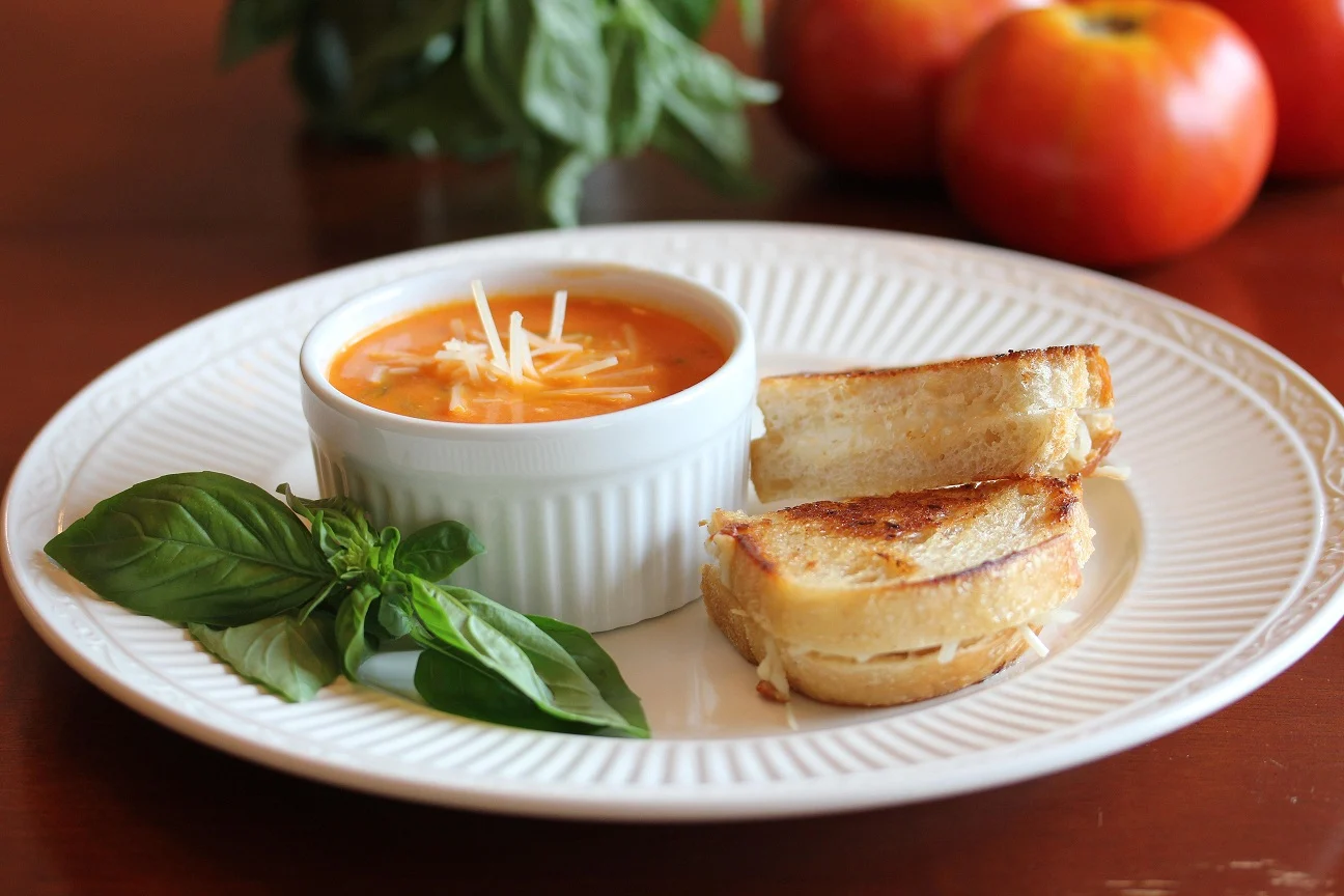Tomato basil soup and grilled cheese dipper on a plate garnished with fresh basil