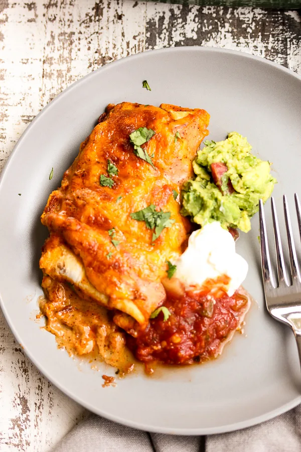 Overhead photo of Chicken Enchiladas served with guacamole, sour cream and salsa