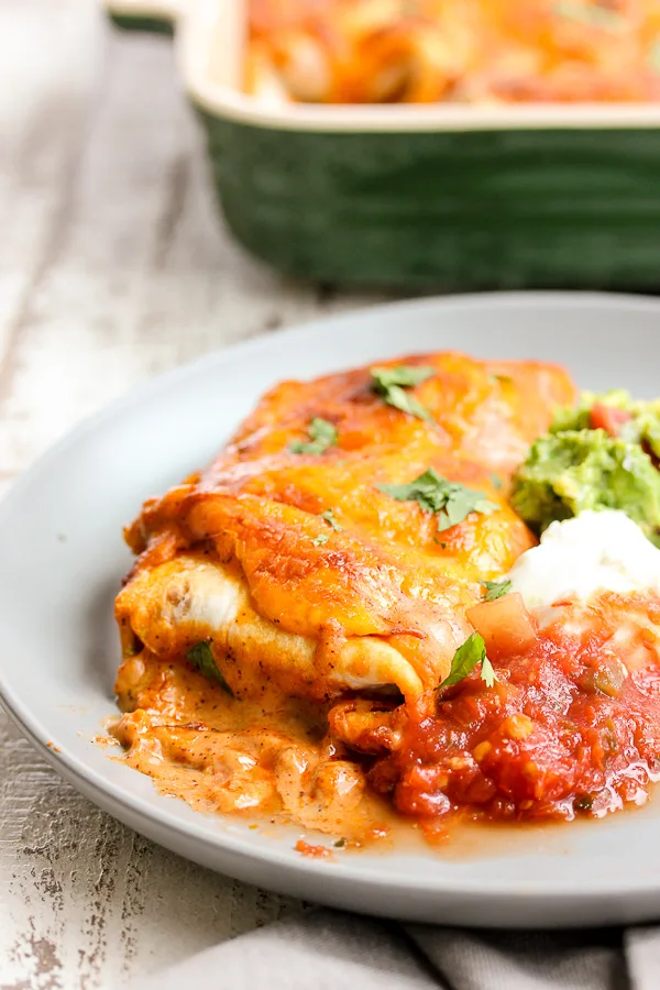 Close up of plated Chicken Enchiladas with the pan of enchiladas in the background