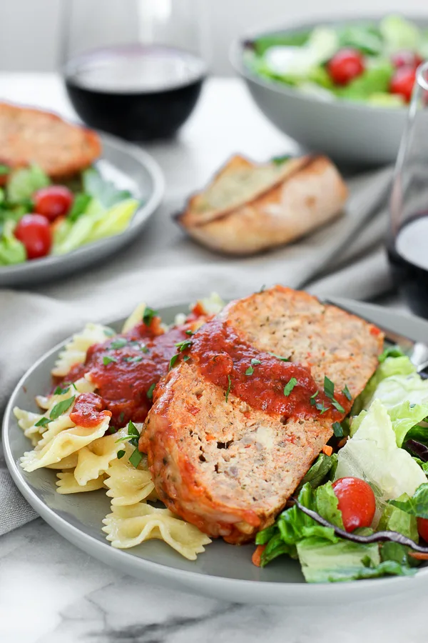 Vertical shop of Italian turkey meatloaf plated with pasta, salad and wine