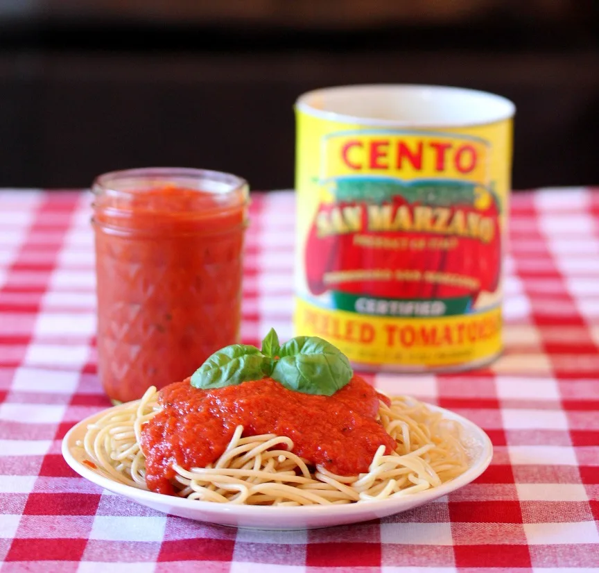 Tomato sauce plated over spaghetti with jar of finished sauce and tomato can in the background