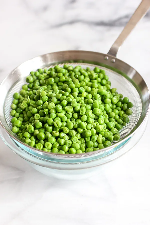 Cooked peas ins strainer being drained after microwaving