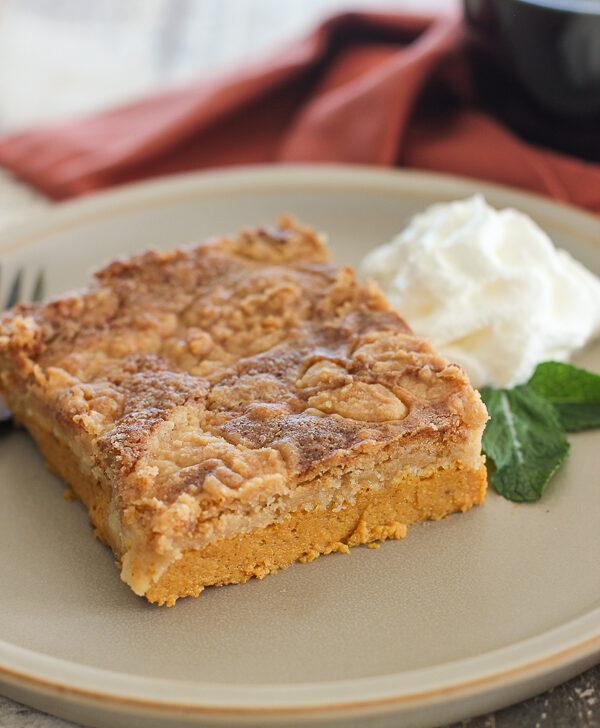 Close up of a slice of pumpkin dump cake served on a plate and garnished with whipped cream and fresh mint