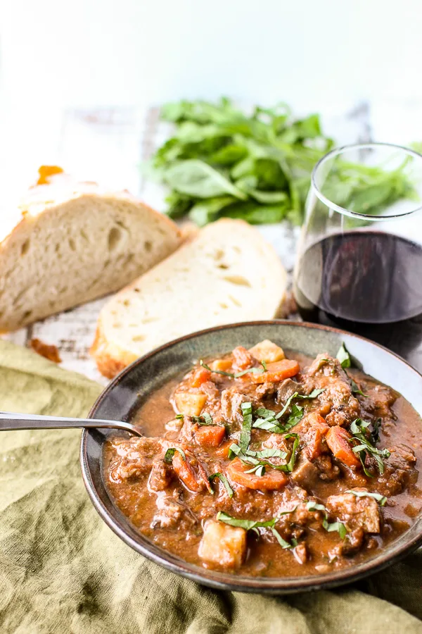 Beef Stew served in a bowl along with a glass of wine and bread