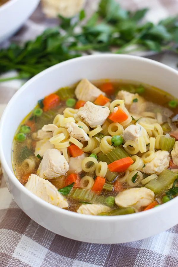 Close up photo showing the detail of the lemon dill chicken noodle soup served in a bowl with fresh parsley in the background.