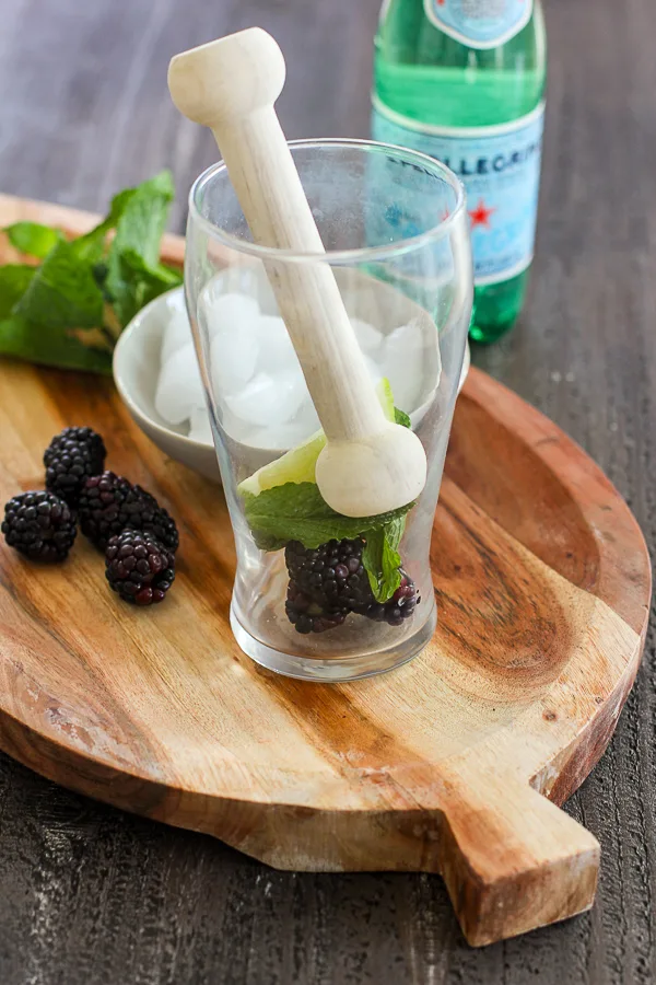 Lime, mint and blackberries in the cocktail glass with a wooden muddler ready to be muddled