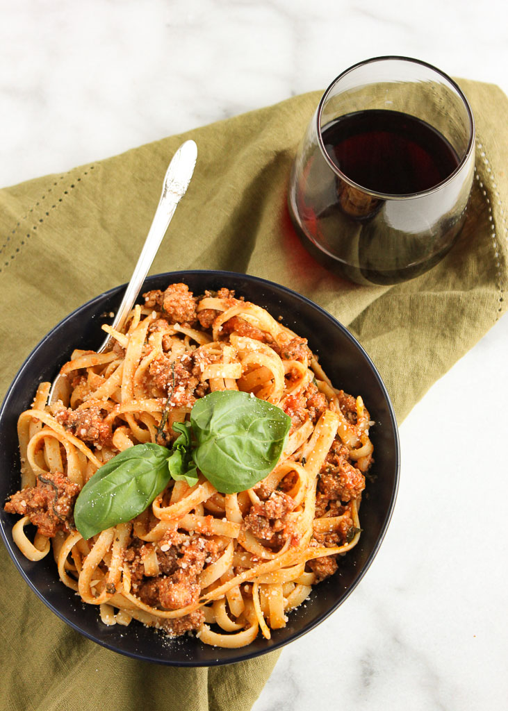 Fettuccine Bolognese served in a bowl with a glass of red wine