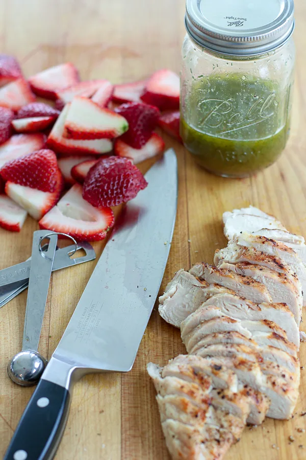 Process photo showing sliced chicken breast, sliced strawberries and dressing in a jar.