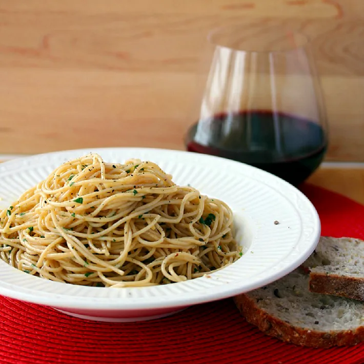 Spaghetti aglio d olio plated with a glass of wine and bread