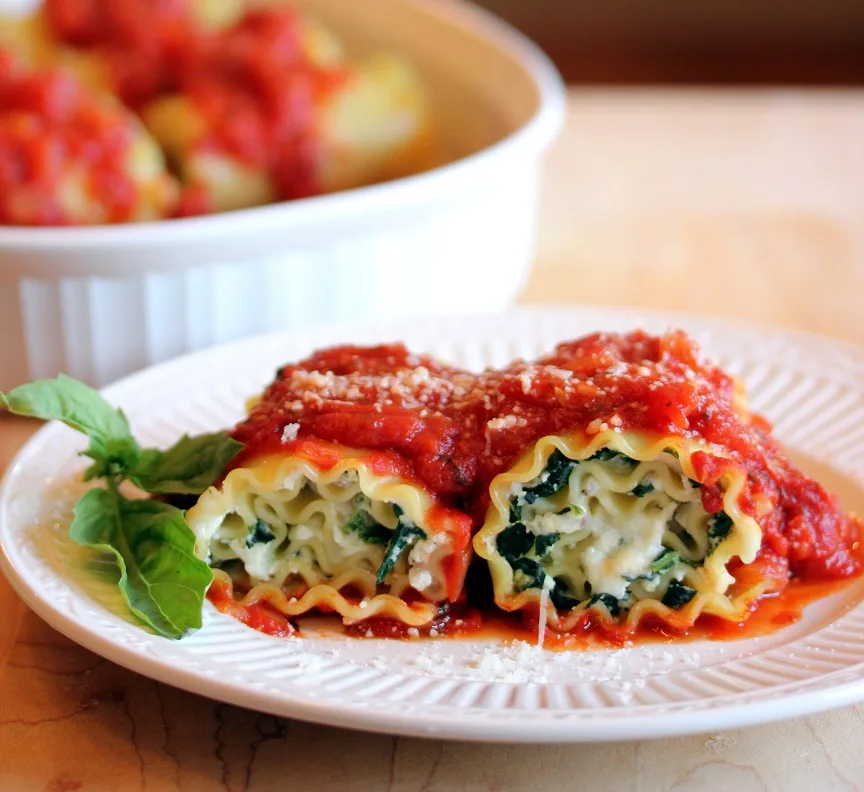 Spinach and cheese lasagna roll ups plated with basil garnish with baking dish in the background 