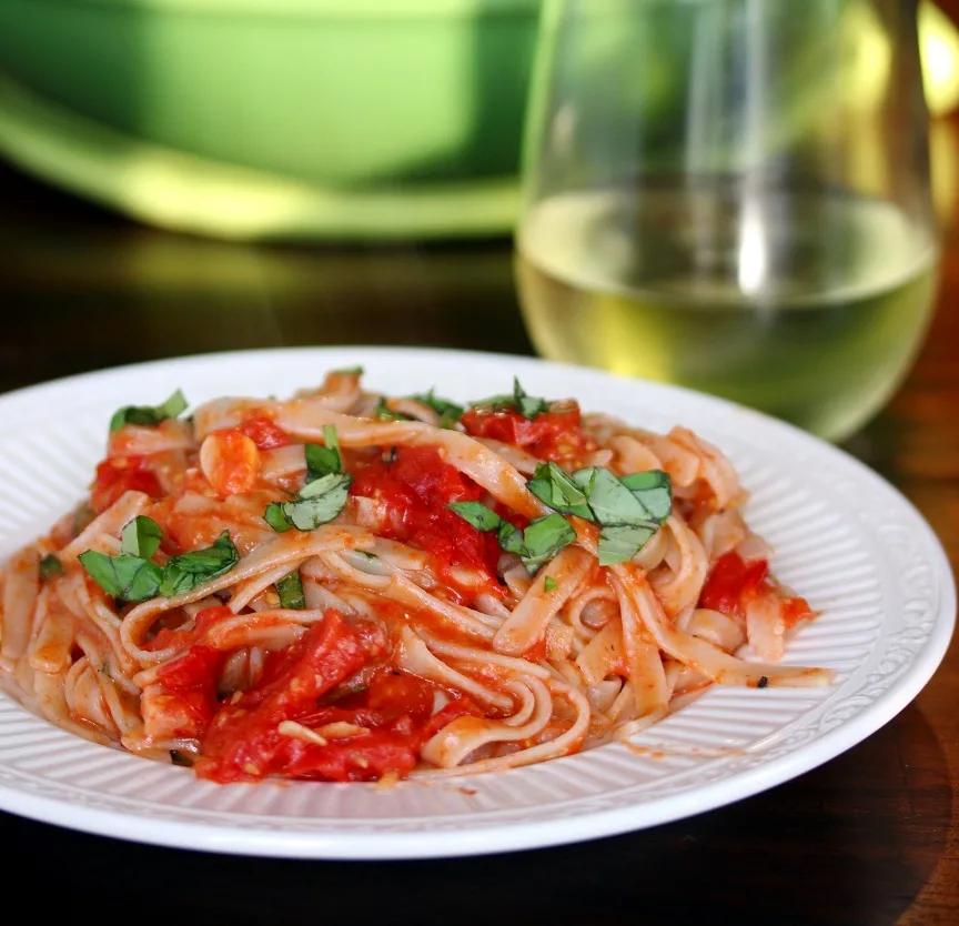 Roasted tomatos and pancetta pasta toss is plated with fettuccine and served with a glass of white wine