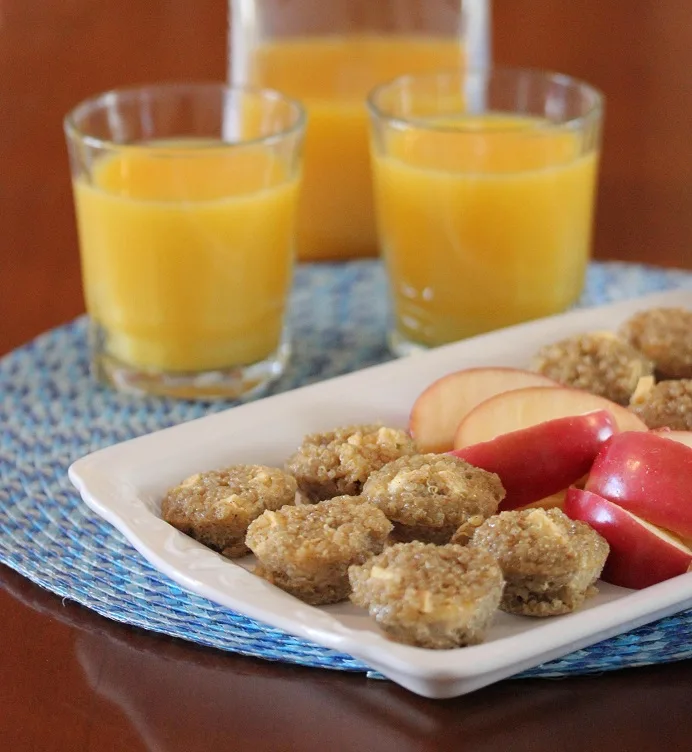 Quinoa apple breakfast bites on a serving platter with apple slices and orange juice in the background
