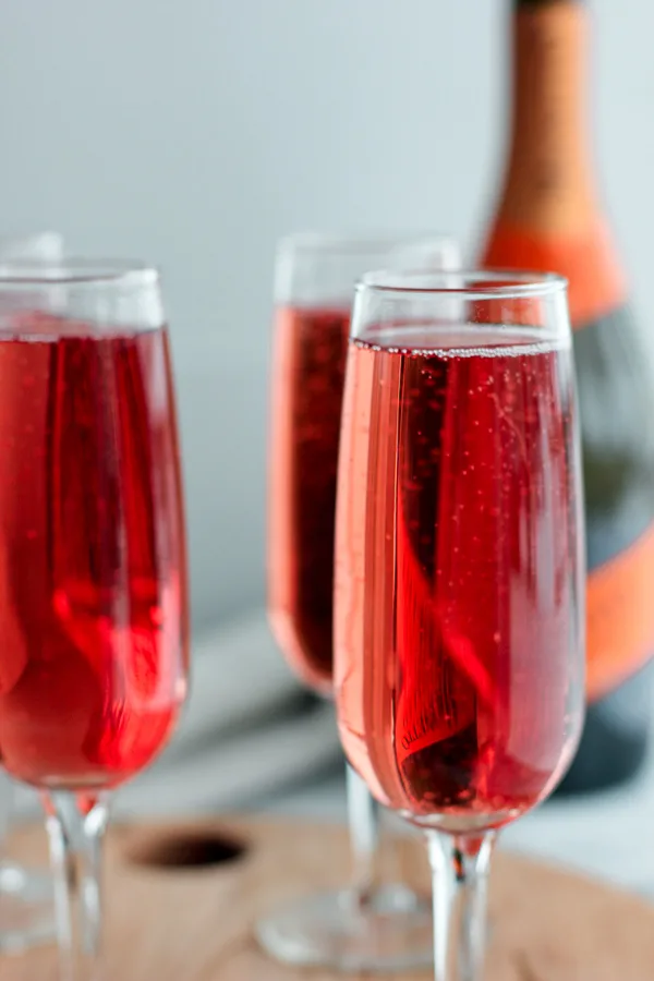 Cranberry-Raspberry Champagne Cocktails in champagne flutes with the bottle of champagne in the background