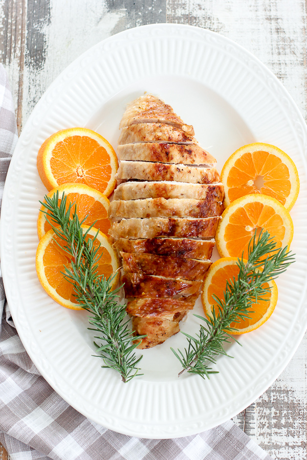 Overhead photo of turkey breast sliced and served on a platter garnished with orang slices and fresh rosemary