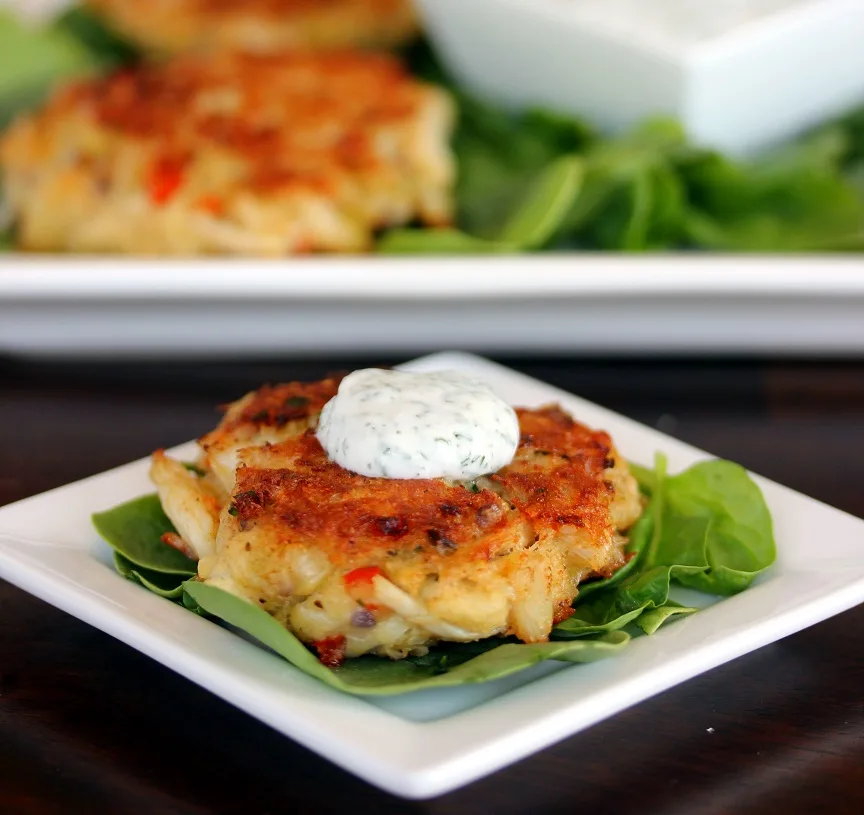 crab cake plated on lettuce leaves and topped with dill sauce