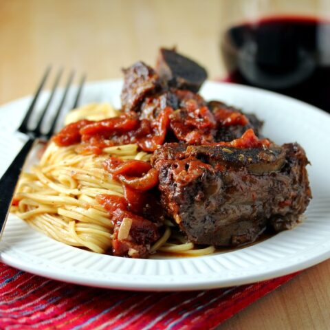 Photo of short ribs served over spaghetti along with a glass of wine