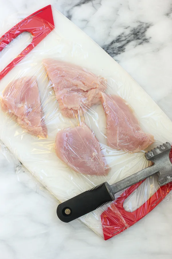 Demonstrating how to pound out the chicken breast on a cutting board with a meat mallet