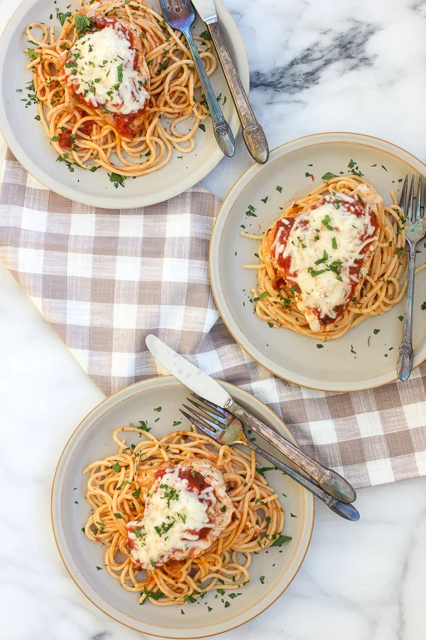 Chicken Parmesan plated on three plates over spaghetti that was tossed with marinara sauce.