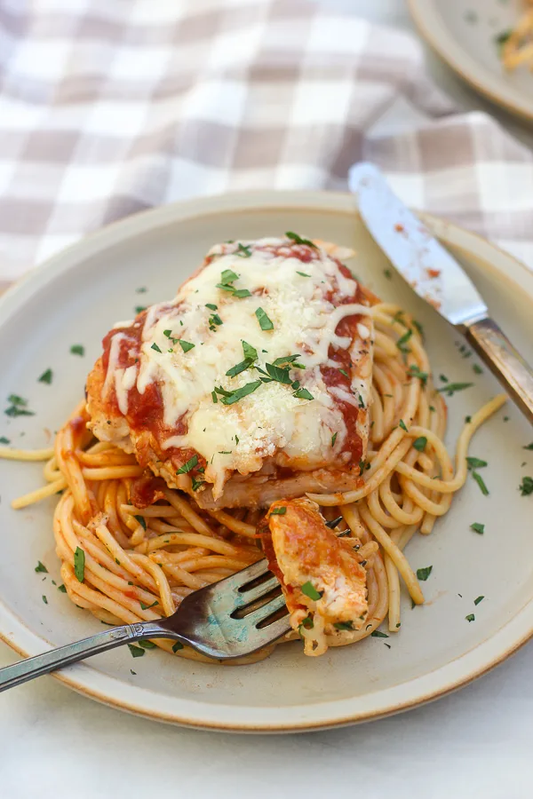 Chicken parmesan showing a fork with a piece of the chicken on it